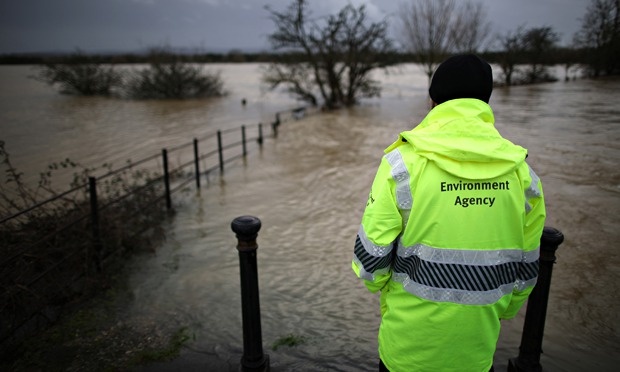 Floods defence budget cuts : An Environment Agency employee looks at flood water from the river Arun